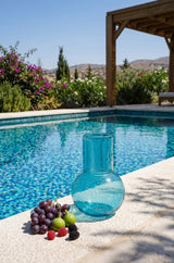 Blue glass vase and fruits on a poolside ledge with a scenic background