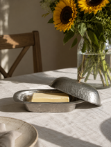 Brass butter dish with a stick of butter on a table with sunflowers in the background