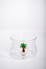 Clear glass bowl with a small palm tree inside on a white background