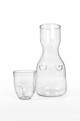 Clear glass carafe and tumbler with face designs on a white background
