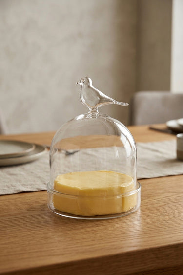 Glass container with a bird on top on a wooden table