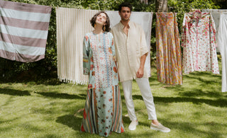 A man and a woman are standing in front of drying clothing