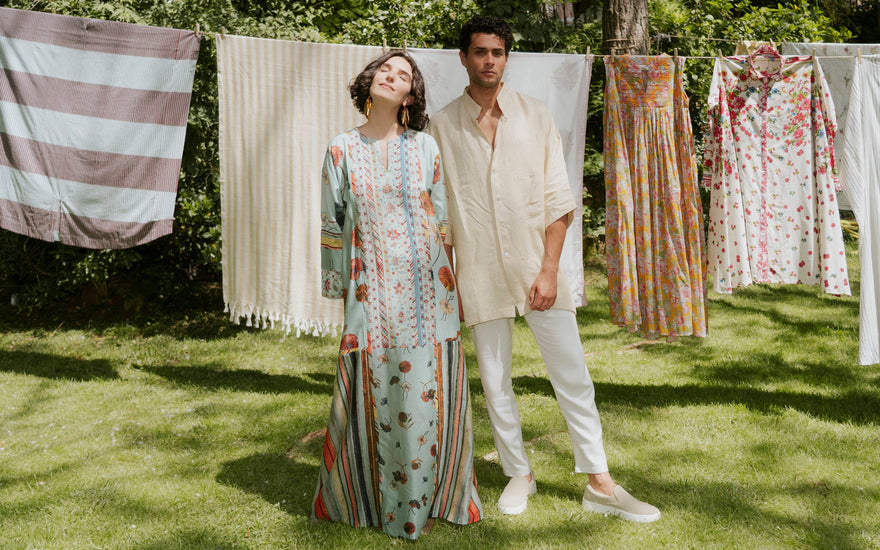 A man and a woman are standing in front of drying clothing