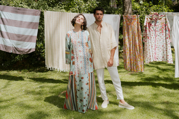 A man and a woman are standing in front of drying clothing