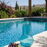Blue glass vase and fruits on a poolside ledge with a scenic background