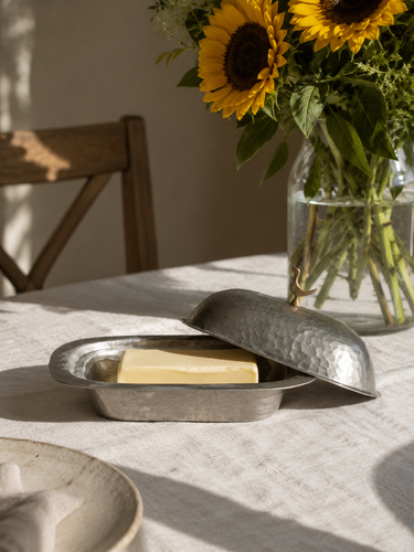 Brass butter dish with a stick of butter on a table with sunflowers in the background