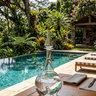Clear glass decanter on a wooden table by a pool with lush greenery in the background