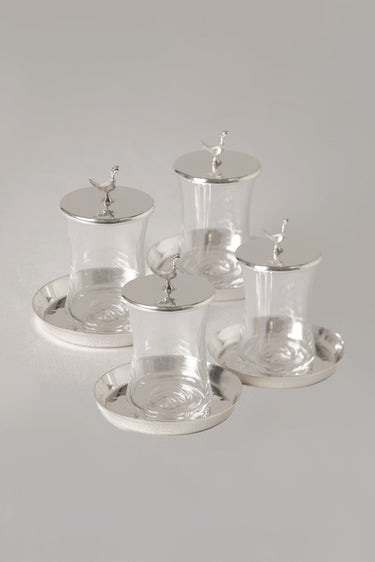 Set of four glass tea cups with silver lids and bases on a gray background