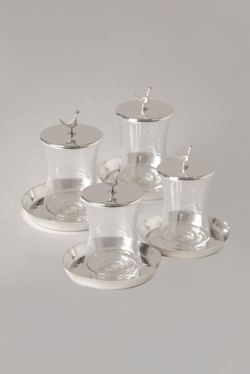 Set of four glass tea cups with silver lids and bases on a gray background