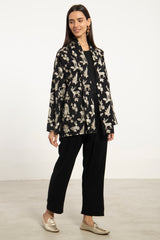 A woman modeling a black long-sleeve blazer with a cream dog pattern, paired with black wide-leg pants and metallic gold loafers, set against a plain white studio background.