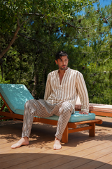 Man in a striped robe sitting on a lounge chair outdoors with trees in the background