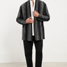 Man wearing a gray patterned blazer over a white shirt with black pants and shoes on a white background