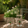 Two glass containers with small tree figurines on a wooden table outdoors.