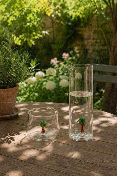 Two glass containers with small tree figurines on a wooden table outdoors.